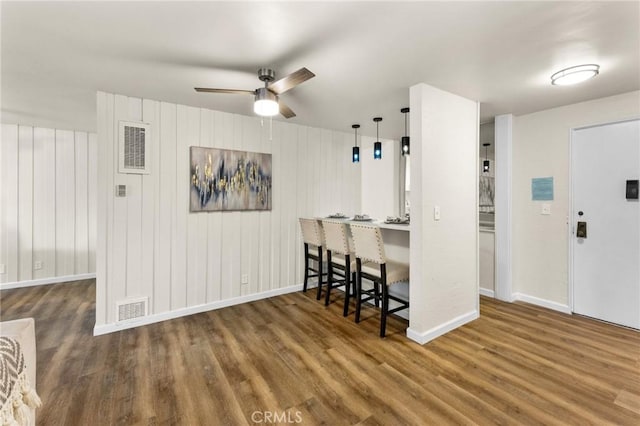 kitchen featuring a breakfast bar, wood-type flooring, ceiling fan, and wood walls