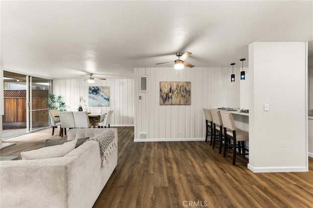 living room featuring ceiling fan, wooden walls, and dark wood-type flooring