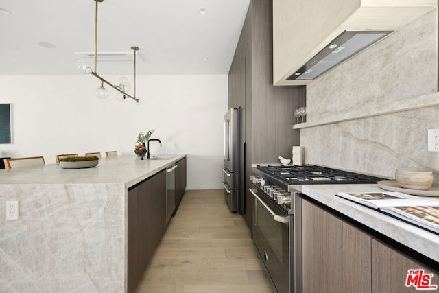 kitchen with pendant lighting, light hardwood / wood-style floors, ventilation hood, a kitchen bar, and appliances with stainless steel finishes