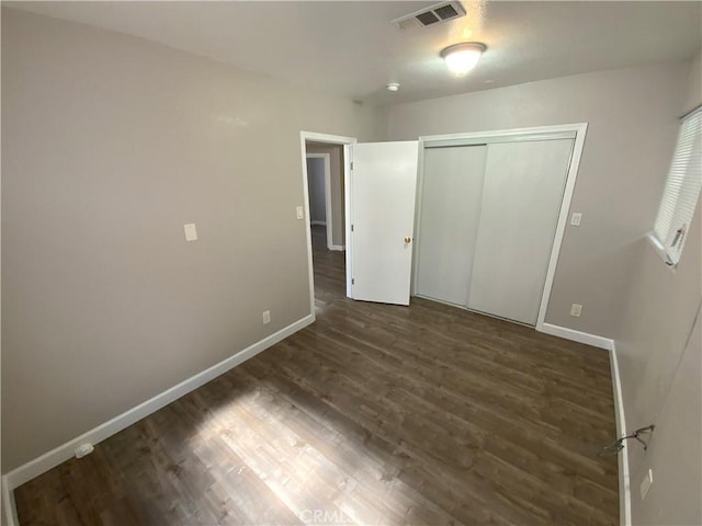 unfurnished bedroom with wood finished floors, baseboards, a closet, and visible vents