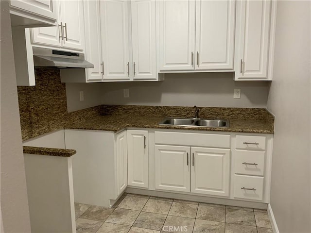kitchen with under cabinet range hood, white cabinetry, a sink, and dark stone counters