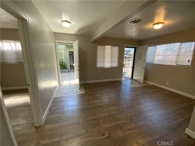interior space with wood finished floors, baseboards, beam ceiling, and visible vents