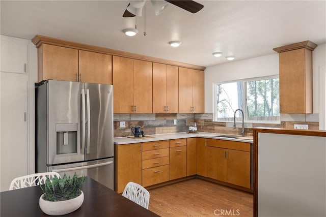 kitchen featuring sink, stainless steel refrigerator with ice dispenser, decorative backsplash, ceiling fan, and light wood-type flooring