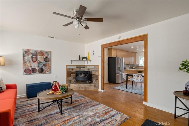 living room with ceiling fan, a wood stove, and light hardwood / wood-style flooring