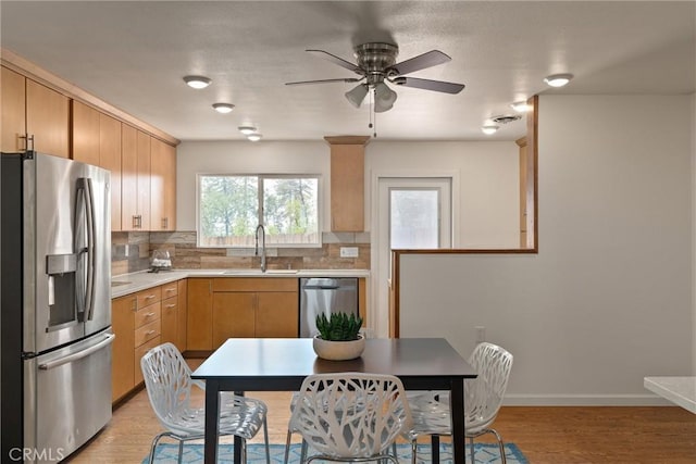 kitchen featuring backsplash, sink, light hardwood / wood-style flooring, ceiling fan, and stainless steel appliances