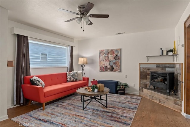 living room with a wood stove, ceiling fan, and wood-type flooring