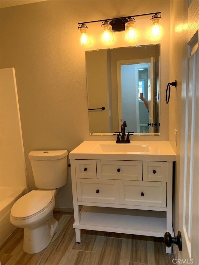 full bath featuring toilet, a bath, wood finished floors, and vanity