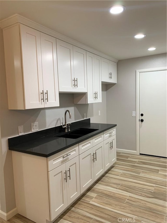 kitchen with white cabinetry, recessed lighting, dark countertops, a sink, and light wood finished floors