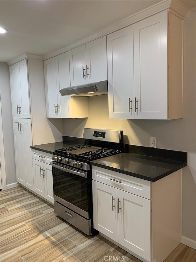 kitchen with stainless steel gas stove, light wood-type flooring, white cabinetry, under cabinet range hood, and dark countertops