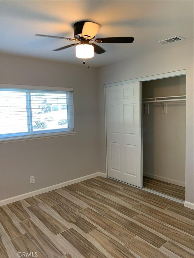 unfurnished bedroom with light wood-type flooring, a closet, baseboards, visible vents, and ceiling fan