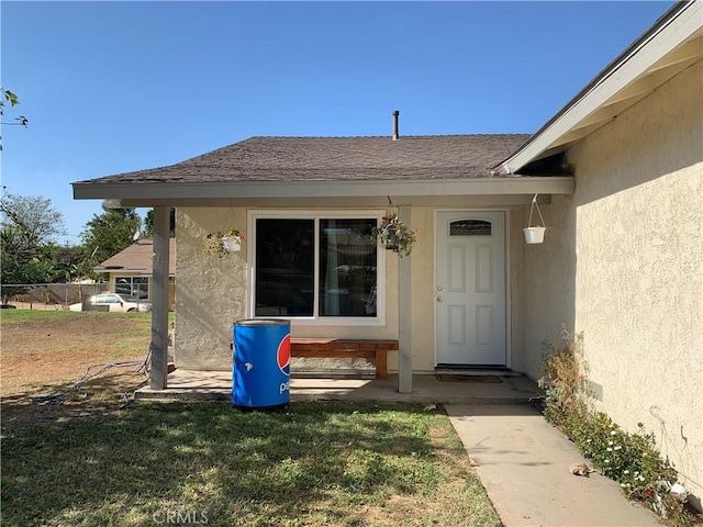 property entrance with a shingled roof, a lawn, and stucco siding