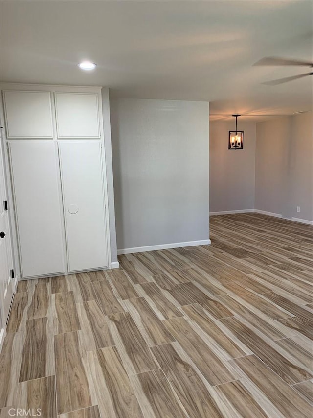 interior space with light wood-style floors, ceiling fan with notable chandelier, baseboards, and recessed lighting