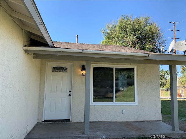 entrance to property featuring stucco siding and roof with shingles