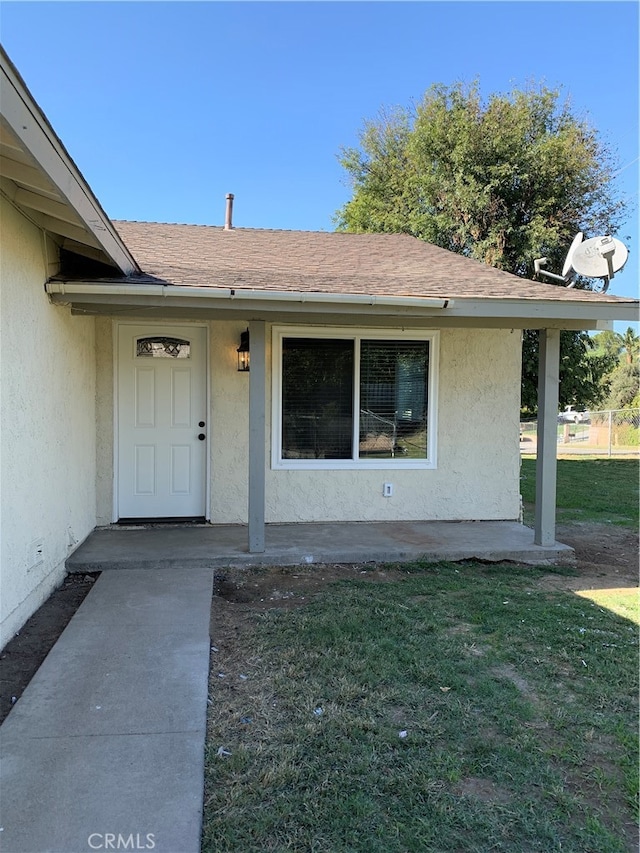 doorway to property featuring a yard, a shingled roof, and stucco siding