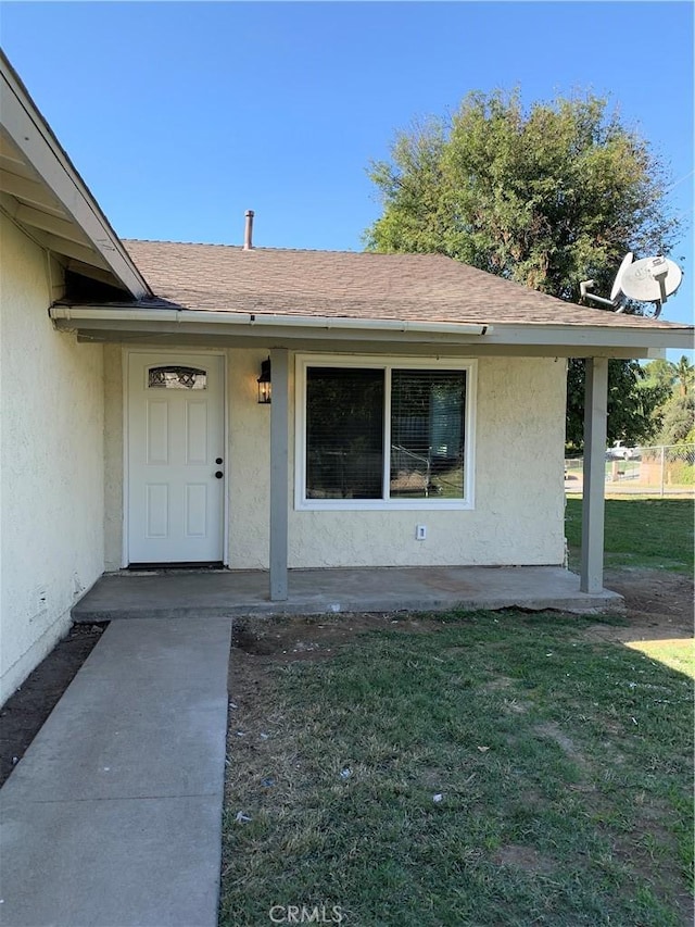 view of exterior entry with a yard, a shingled roof, and stucco siding