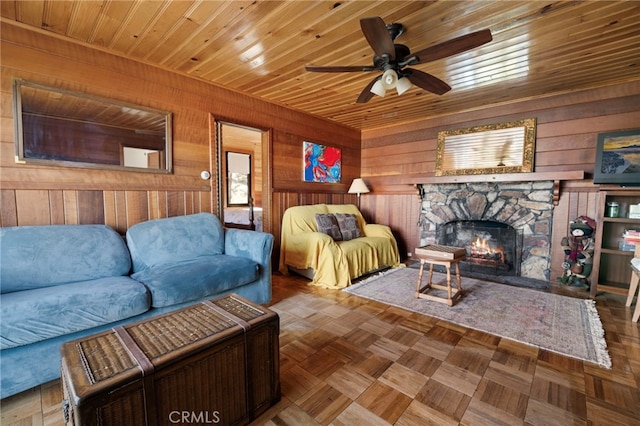 living room with ceiling fan, wood walls, parquet floors, a stone fireplace, and wooden ceiling