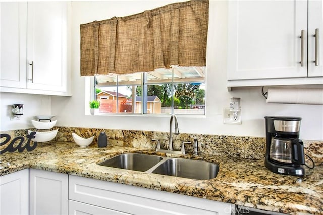 kitchen featuring dishwasher, light stone counters, white cabinetry, and sink