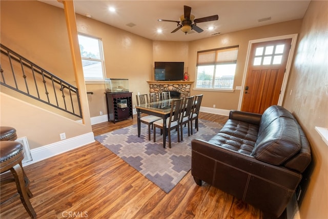 dining space with ceiling fan, a stone fireplace, hardwood / wood-style flooring, and a healthy amount of sunlight