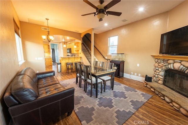 dining area featuring ceiling fan with notable chandelier, a fireplace, and hardwood / wood-style flooring