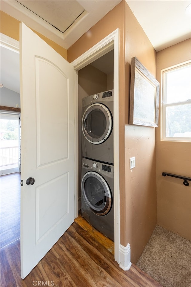 laundry room featuring dark hardwood / wood-style floors, stacked washer and dryer, and a wealth of natural light