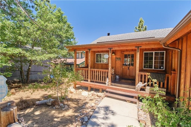 doorway to property featuring a shingled roof, fence, a porch, and board and batten siding