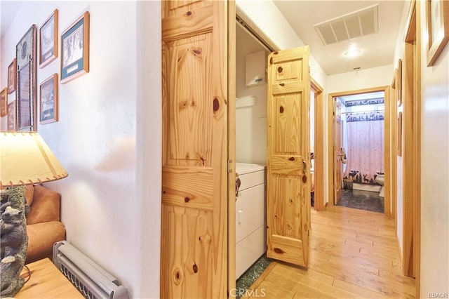 hall featuring light wood-style floors, a baseboard radiator, visible vents, and washer / dryer