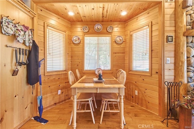 dining area with light wood finished floors, wood ceiling, and wooden walls