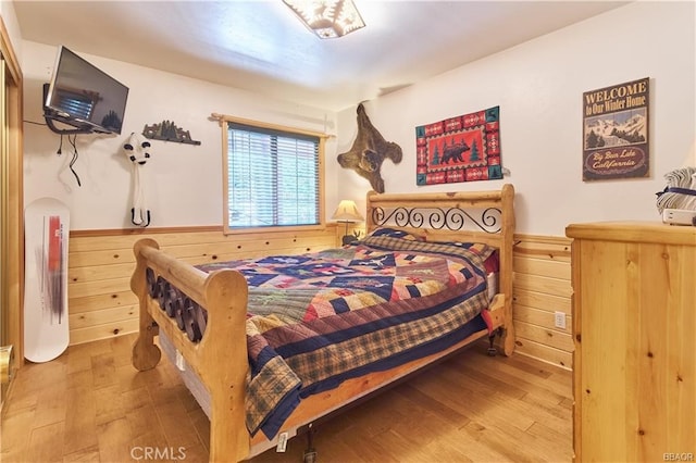 bedroom featuring a wainscoted wall, wood finished floors, and wooden walls