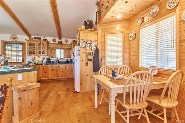 kitchen featuring beam ceiling, glass insert cabinets, freestanding refrigerator, light wood-style floors, and wooden walls