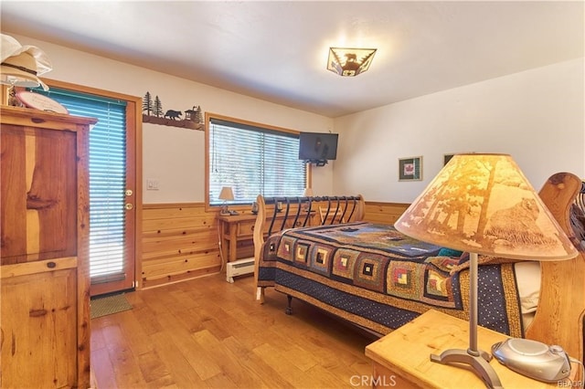 bedroom with a baseboard radiator, a wainscoted wall, wood walls, and wood finished floors