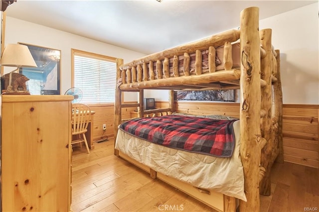 bedroom with light wood-style floors, wooden walls, and wainscoting