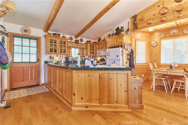 kitchen featuring lofted ceiling with beams, a peninsula, white appliances, light wood-style floors, and glass insert cabinets