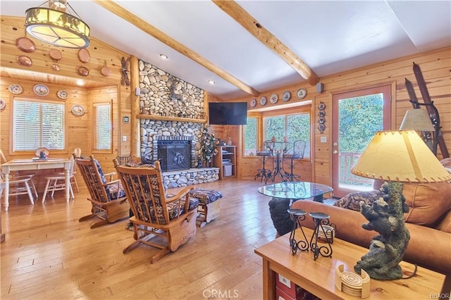 living area with lofted ceiling with beams, a stone fireplace, wood finished floors, and wooden walls