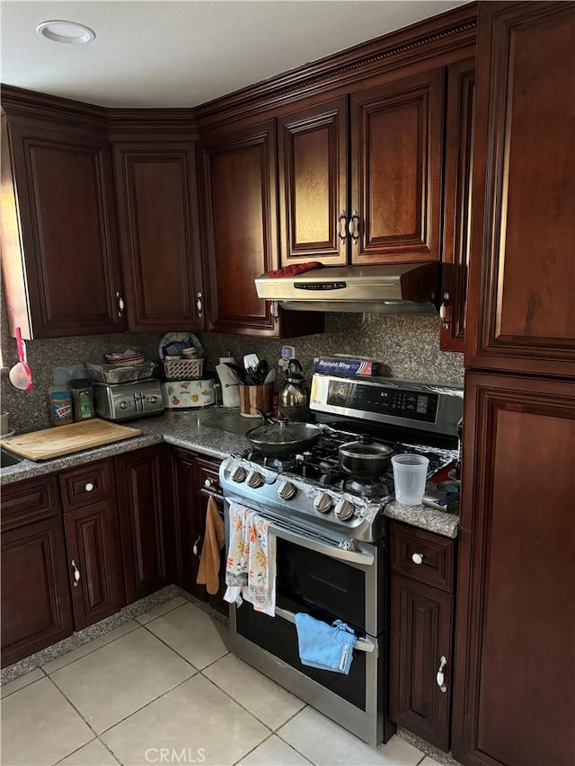 kitchen featuring backsplash, light tile patterned floors, under cabinet range hood, and range with two ovens