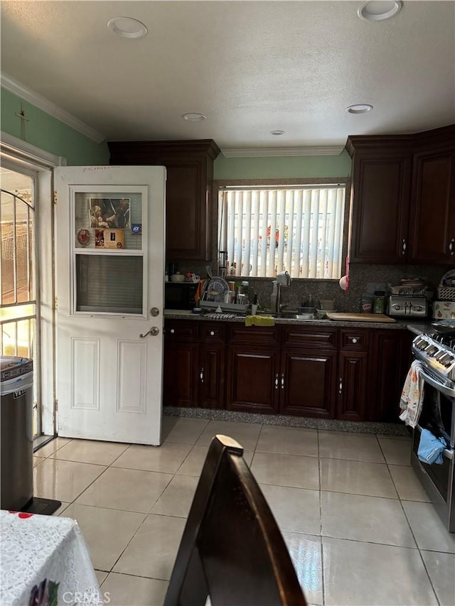 kitchen featuring crown molding, dark brown cabinetry, gas range, tasteful backsplash, and a sink