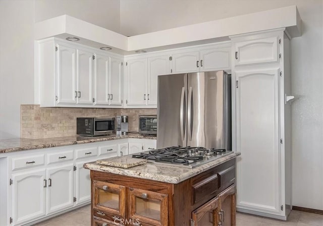 kitchen featuring stainless steel appliances, white cabinetry, light stone countertops, and backsplash