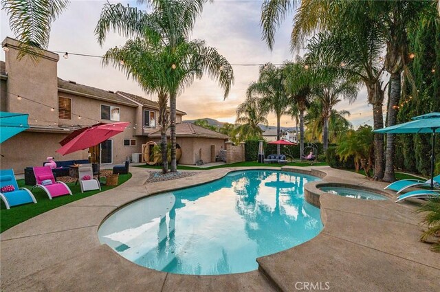 pool at dusk with a patio area and a pool with connected hot tub