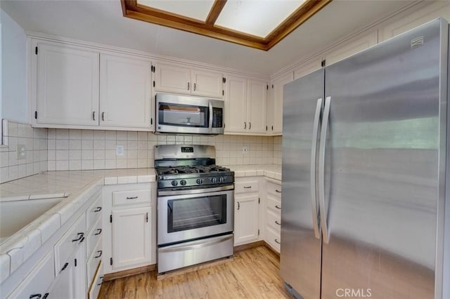 kitchen featuring light wood-type flooring, tile counters, white cabinetry, stainless steel appliances, and backsplash