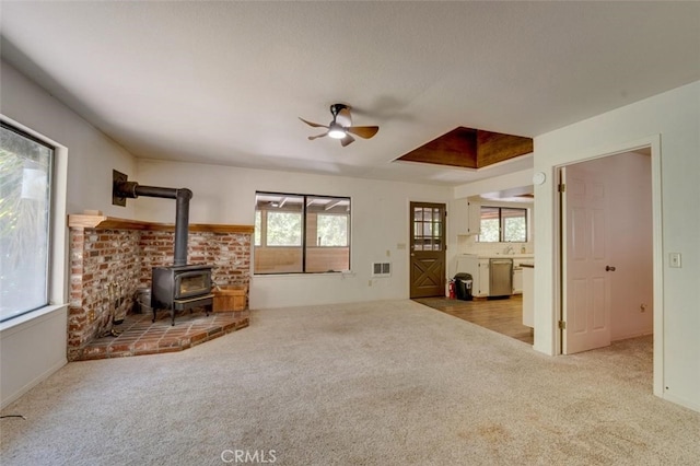 living room with ceiling fan, light colored carpet, brick wall, and a wood stove