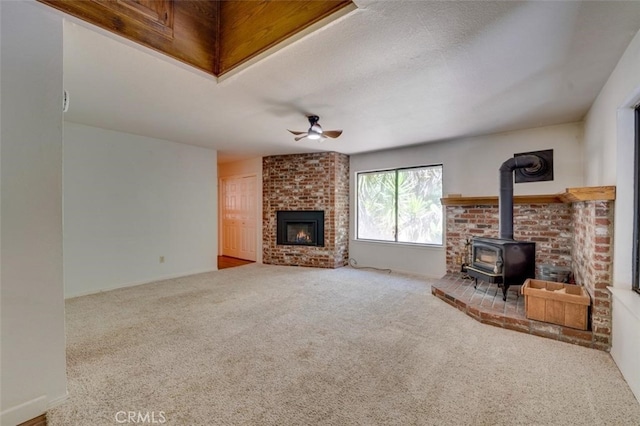 unfurnished living room featuring ceiling fan, a textured ceiling, a wood stove, and carpet