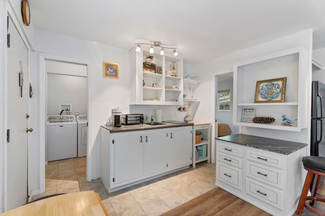 kitchen featuring sink, white cabinetry, washer and clothes dryer, light wood-type flooring, and black refrigerator