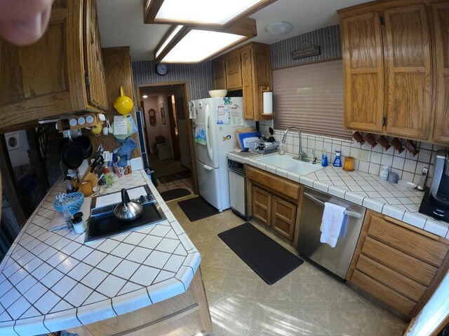 kitchen with dishwasher, sink, white fridge, backsplash, and tile countertops