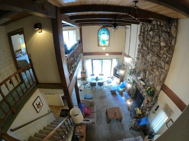 living room with ceiling fan, beam ceiling, a stone fireplace, high vaulted ceiling, and wooden ceiling