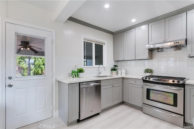 kitchen featuring gray cabinets, stainless steel appliances, light countertops, under cabinet range hood, and a sink