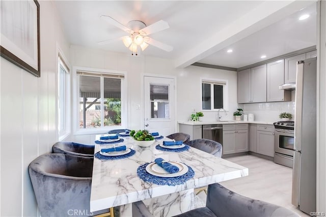 kitchen featuring a breakfast bar area, beamed ceiling, gray cabinets, and appliances with stainless steel finishes