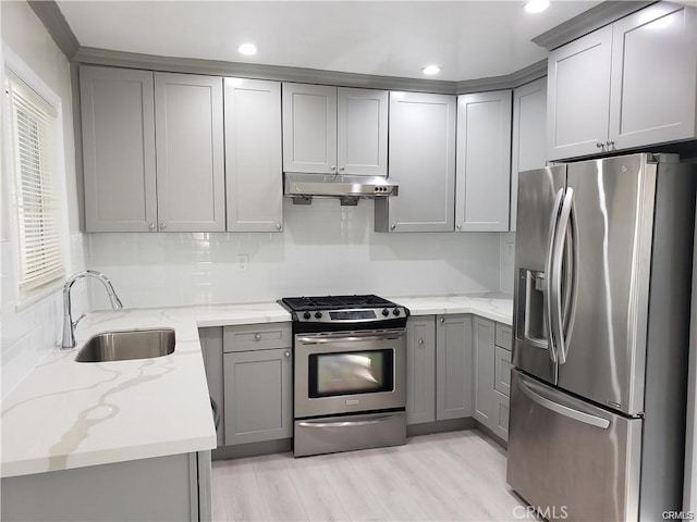 kitchen featuring appliances with stainless steel finishes, light stone counters, gray cabinetry, under cabinet range hood, and a sink