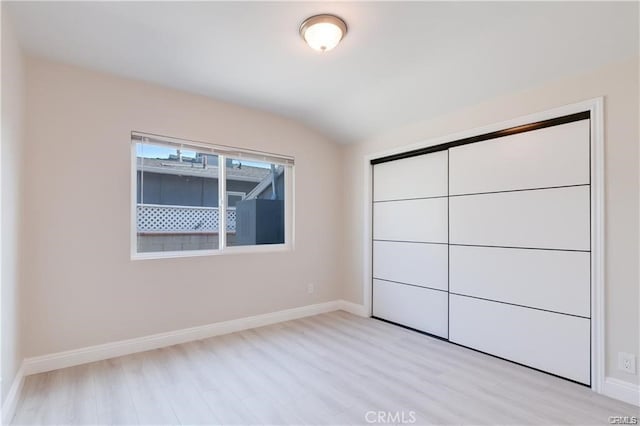 unfurnished bedroom featuring light wood-style floors, lofted ceiling, a closet, and baseboards