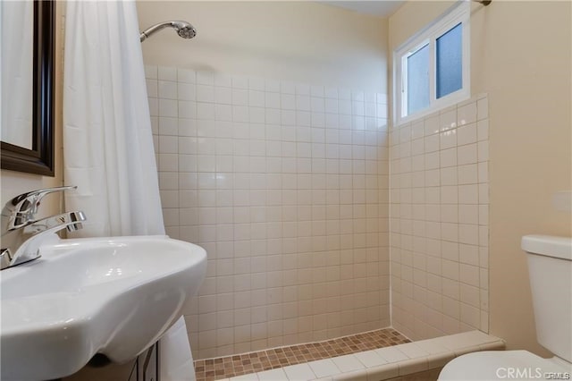 bathroom with tiled shower, a sink, and toilet