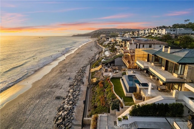 aerial view at dusk featuring a residential view, a water view, and a beach view