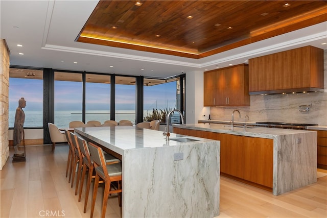 kitchen featuring brown cabinetry, a raised ceiling, wooden ceiling, a large island, and a sink